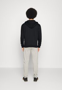 Felpa nera con cappuccio e lacci, pantaloni della tuta grigi e sneakers nere. Il tessuto sembra morbido, con una vestibilità rilassata e un design semplice.