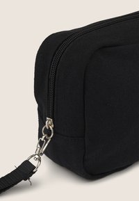 Borsa nera in canvas con una superficie testurizzata, dotata di una zip argentata e di un gancio metallico di attacco su una tracolla robusta per il trasporto.