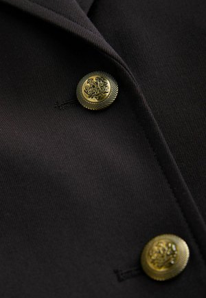 Schwarzer Stoffblazer mit goldenen, strukturierten Knöpfen mit filigranen Designs und maßgeschneiderter Passform, die scharfe Revers und klare Linien betont.