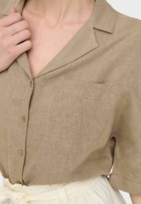 Camicia a maniche corte in lino marrone chiaro con taschino, colletto e chiusura a bottoni. Tessuto morbido, design casual.