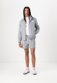 Gray and white striped lightweight jacket with a relaxed fit, paired with matching shorts. Includes drawstring and subtle brand logo detail.