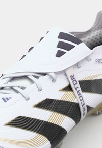 White and black soccer cleat with a textured upper, gold accents, laces, and a fold-over tongue marked "PREDATOR."