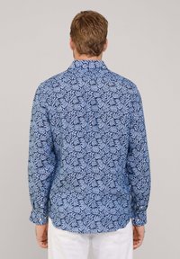 Camisa de manga larga con un patrón de hojas azules sobre un fondo claro, hecha de una tela suave. Botones en los puños y en la parte posterior del cuello.