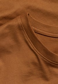 Brunt bomulds T-shirt stof, der viser et nærbillede af den ribbede halslinning og den glatte tekstur, med synlige sømme.