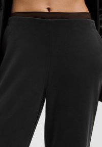 Čierne tepláky vyrobené z mäkkej látky s hnedým pásom. Majú hladkú textúru a rovný strih.