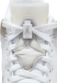 Baskets blanches avec languette en tissu texturé, lacets blancs attachés à travers un verrou de lacet en plastique affichant un logo Jumpman discret.