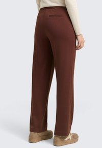 Braune weite Hosen mit glatter Textur, elastischem Bund und Gesäßtaschen, kombiniert mit hellbraunen Sneakers.