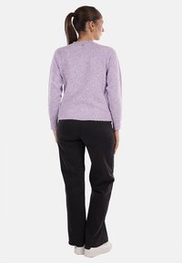 Maglione lilla con una finitura testurizzata, scollatura rotonda e maniche lunghe, abbinato a pantaloni neri a gamba dritta e sneakers bianche.