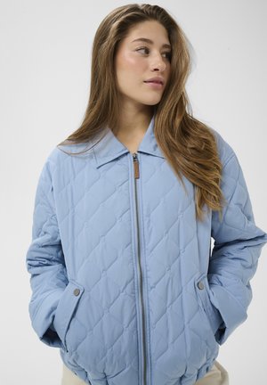 Chaqueta acolchada azul claro con cierre de cremallera, gran cuello y bolsillos laterales con botones de presión, que muestra una tela lisa y texturizada.