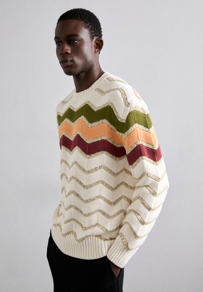 Adīta džemperis ar zigzaga rakstu krēmkrāsā, apelsīnu, zaļā, sarkanā un zelta krāsā, ar ribotām piedurknēm un apakšmalu. Tekstūrēts un silts dizains.