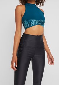 Turkusowy crop top z wysokim dekoltem i czarną opaską "NIKE PRO". Połączony z czarnymi legginsami o wysokim stanie, o gładkiej, błyszczącej fakturze.