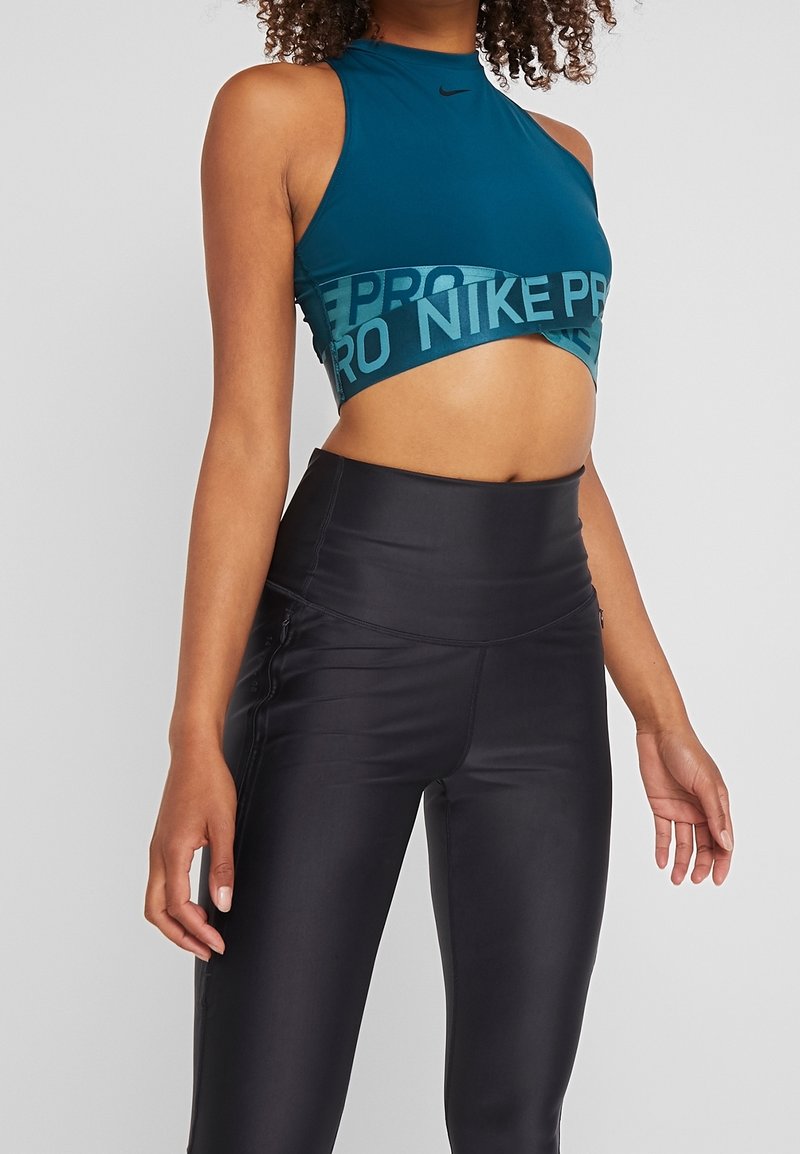 Turkusowy crop top z wysokim dekoltem i czarną opaską "NIKE PRO". Połączony z czarnymi legginsami o wysokim stanie, o gładkiej, błyszczącej fakturze.