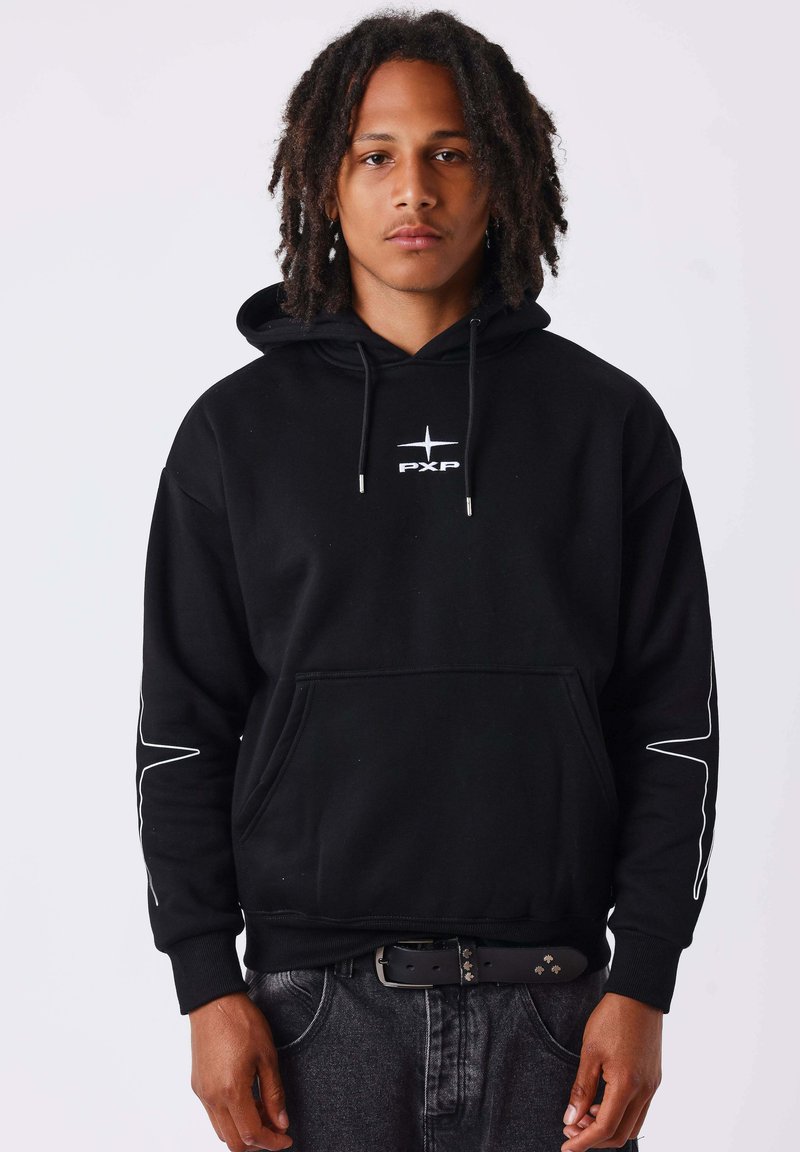 Jeune homme avec des dreadlocks aux épaules portant un sweat à capuche noir avec un logo PXP blanc et des motifs sur les manches, debout devant un fond uni.