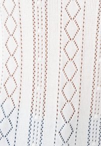 De gebreide stof heeft een witte basis met diamanten en geometrische patronen in lichtbruin en blauw, die een gestructureerd, verticaal strepenpatroon creëren.