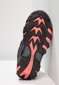 Scarpa sportiva nera con suola spessa e testurizzata, presenta dettagli rosa e un motivo a zigzag. Progettata per la trazione e la durata.