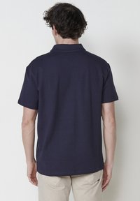 Polo shirt bleu marine à manches courtes avec un motif texturé, présentant un col et un ourlet droit, vu de l'arrière.