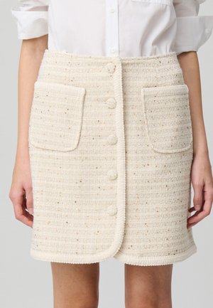Gonna di tweed bianca con riflessi dorati, dotata di due grandi tasche frontali e cinque bottoni di chiusura, rifinita con un'orlo texturizzato.