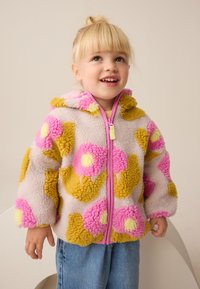 Veste polaire à motif floral rose et jaune, avec capuche et fermeture éclair frontale, portée par un enfant avec un jean bleu.