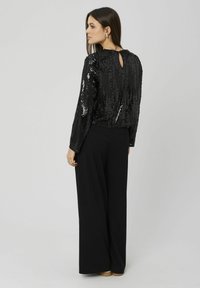 Haut en sequins noirs à manches longues, détail d'ouverture dans le dos, associé à un pantalon noir à jambes larges. Texture lisse et finition brillante.
