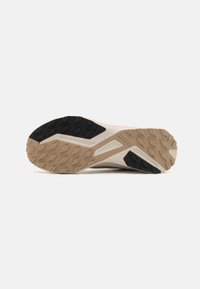 Semelle de chaussure de trail en beige et noir. Comprend du caoutchouc texturé pour l'adhérence, un design profilé et un motif de semelle pour la traction.