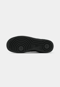 Semelle noire de basket Nike avec des motifs de bande de roulement circulaires et le logo Nike embossé au centre.