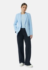 Lichtblauwe blazer met gestructureerde schouders, gecombineerd met een gestreepte blauw-witte top en donkerwijdvallende jeans. Witte sneakers maken de outfit compleet.