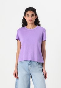 Kortermet, avslappet T-skjorte i lavendel i myk stoff med rund hals, kombinert med lyse høytaljede jeans.