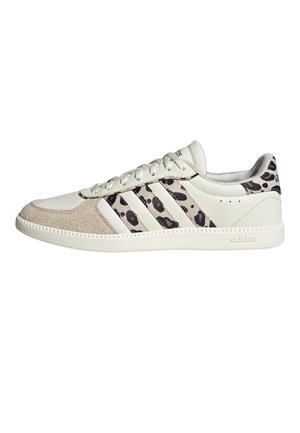 Niski biały sneaker Adidas z beżowym zamszowym noskiem, czarnym nadrukiem w cętki na paskach i pięcie oraz białą gumową podeszwą.