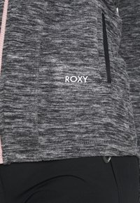 Gray Roxy jacket with a textured pattern, pink zipper, and black accents. Features include side pockets and a snug fit design.