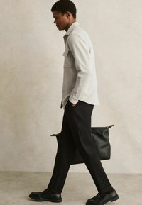 Cămașă gri cu guler, cu un buzunar frontal, pantaloni negri tapered și pantofi negri. O geantă din piele neagră atârnă de umăr.