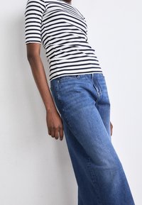 Randig, figurnära topp i marinblå och vit bomull, kombinerad med vida blå denimjeans. Klädesplagget har korta ärmar och en naturlig textur.