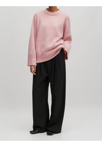 Helles pinkes Sweatshirt mit Rundhalsausschnitt, gerippten Bündchen und lockerer Passform, kombiniert mit schwarzen weit geschnittenen Hosen und glänzenden schwarzen Schuhen.