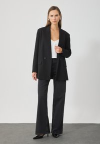 Μαύρο κοστούμι σακάκι με διπλά κουμπιά, δύο μπροστινές τσέπες, σε συνδυασμό με ψηλόμεσα σκούρα τζιν και μαύρες μυτερές γόβες.