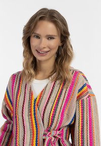 Cardigan a maglia colorato con varie righe orizzontali in rosa, arancione, blu e giallo. Presenta una cintura da annodare in vita e maniche larghe.