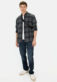 Plaid flannel skjorte i sort og grå, knappet, lagd over en hvid t-shirt. Mørkeblå jeans og cremefarvede sneakers fuldender outfittet.