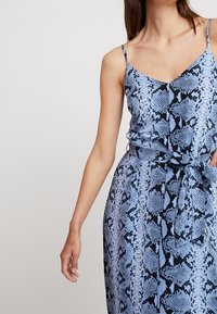 Blue and black snake print dress with adjustable spaghetti straps, flowy fabric, cinched waist, and a tie detail at the waist.