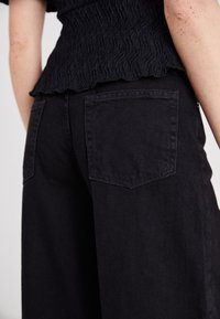 Svarte vide jeans laget av teksturert denim, med to baklommer og en tilpasset midje med en subtil rynke på toppen.