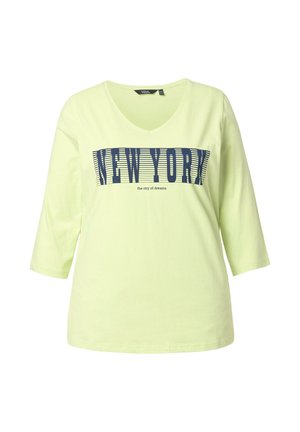 Camiseta de algodón verde claro con cuello en V y mangas tres cuartos, con texto azul: "NEW YORK" y "la ciudad de los sueños" en un diseño a rayas.