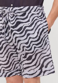 Uimapuvut kevyestä kankaasta, joissa on mustavalkoinen aaltoileva seeprahattu, joustava vyötärö ja sivutaskut.