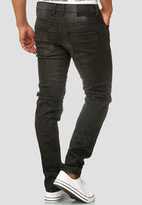 Zwarte denim jeans met een slanke pasvorm, voorzien van vijf zakken, een gladde textuur en een tailleband met merklogo. Draagt witte sneakers.