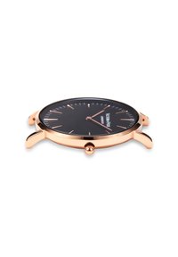 Reloj de metal en tono dorado con una esfera negra, marcadores de hora delgados y una caja redonda. Presenta una corona en el lateral, un acabado suave y garras curvadas.