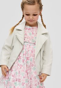 Weiße Kunstleder-Motorradjacke mit Reißverschlussdetails, getragen über einem pastellfarbenen Blumenprint-Kleid mit Spitze und ausgestelltem Rock.