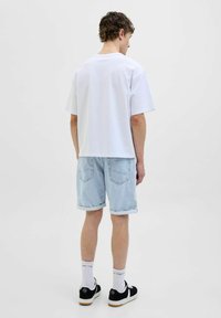 Tricou alb din bumbac, cu mâneci scurte, vedere din spate; asortat cu șorturi din denim albastre deschise, cu manșete rulate, adidași negri și șosete albe.