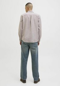 Camisa de manga larga gris claro con cuello abotonado, combinada con jeans azules de corte relajado, vista desde la parte posterior contra un fondo liso.