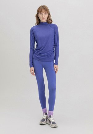 Lila Langarm-Oberteil mit hohem Kragen, kombiniert mit passenden lila Leggings. Beinhaltet hellere lila Akzente an den Knöcheln. Leichter Stoff.