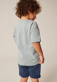 Lys grå t-shirt med korte ærmer og en subtil tekstur, parret med mørkeblå shorts med opkrøllede ben.