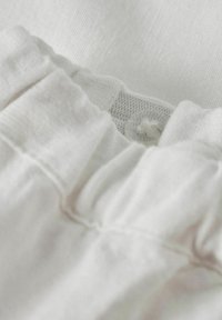 Tissu blanc avec une surface texturée, comportant des détails froncés et une fermeture à bouton. Doux et léger avec une finition lisse.