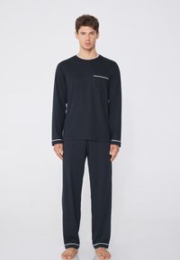 Conjunto de loungewear de dos piezas en azul marino, top de manga larga con ribete blanco y bolsillo, pantalones a juego con dobladillos en los puños, textura de tela suave.