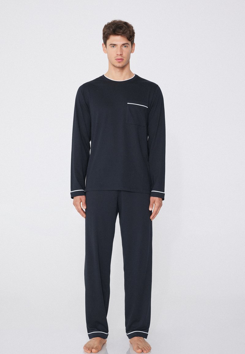 Conjunto de loungewear de dos piezas en azul marino, top de manga larga con ribete blanco y bolsillo, pantalones a juego con dobladillos en los puños, textura de tela suave.