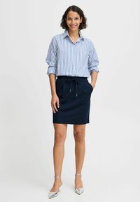Cămașă cu dungi lungi, albă și albastră, purtată împreună cu o fustă în nuanță de marină, cu șnur. Pantofii cu toc subțire, argintii, completează ținuta.